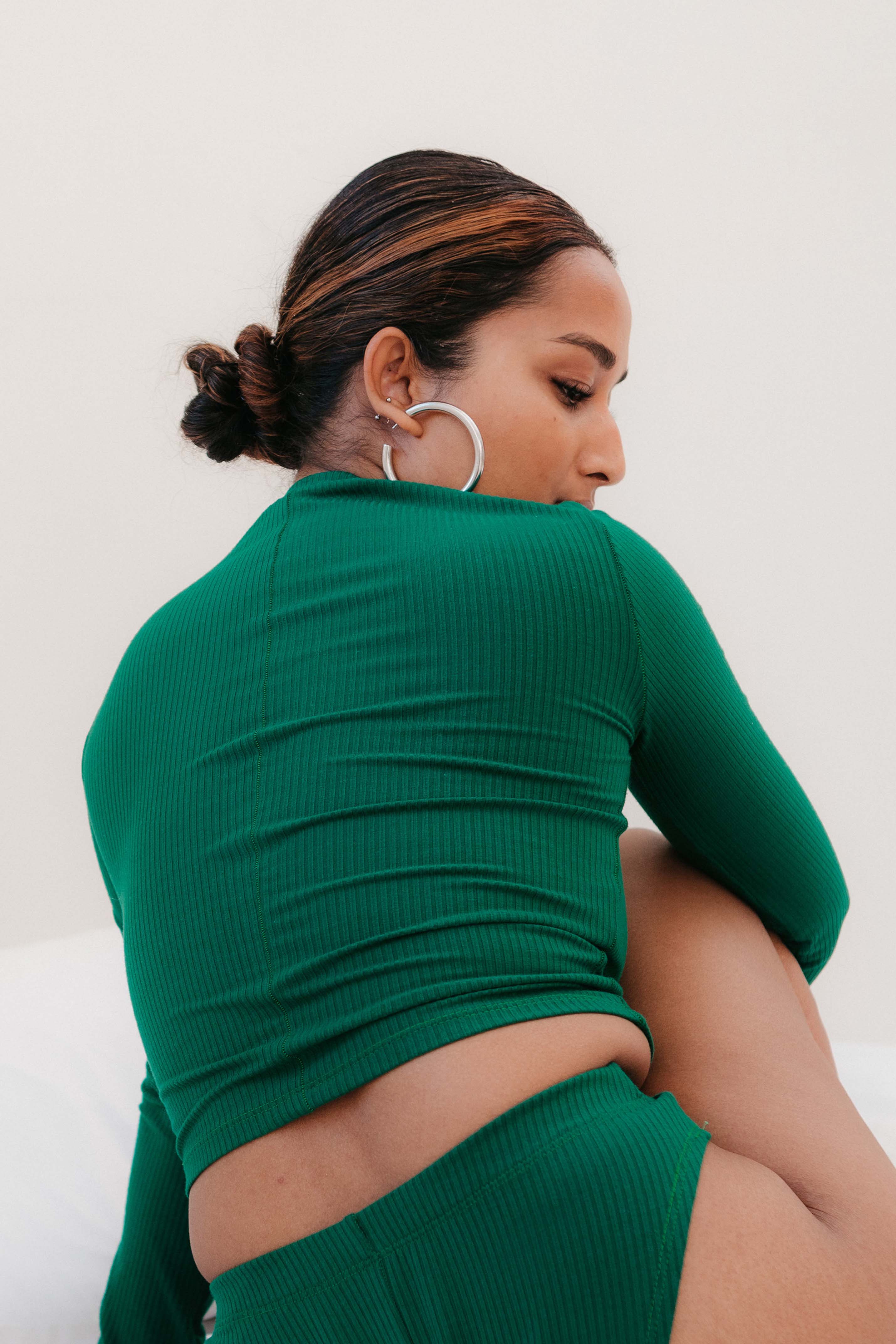 Model sits on floor in a green long sleeve top