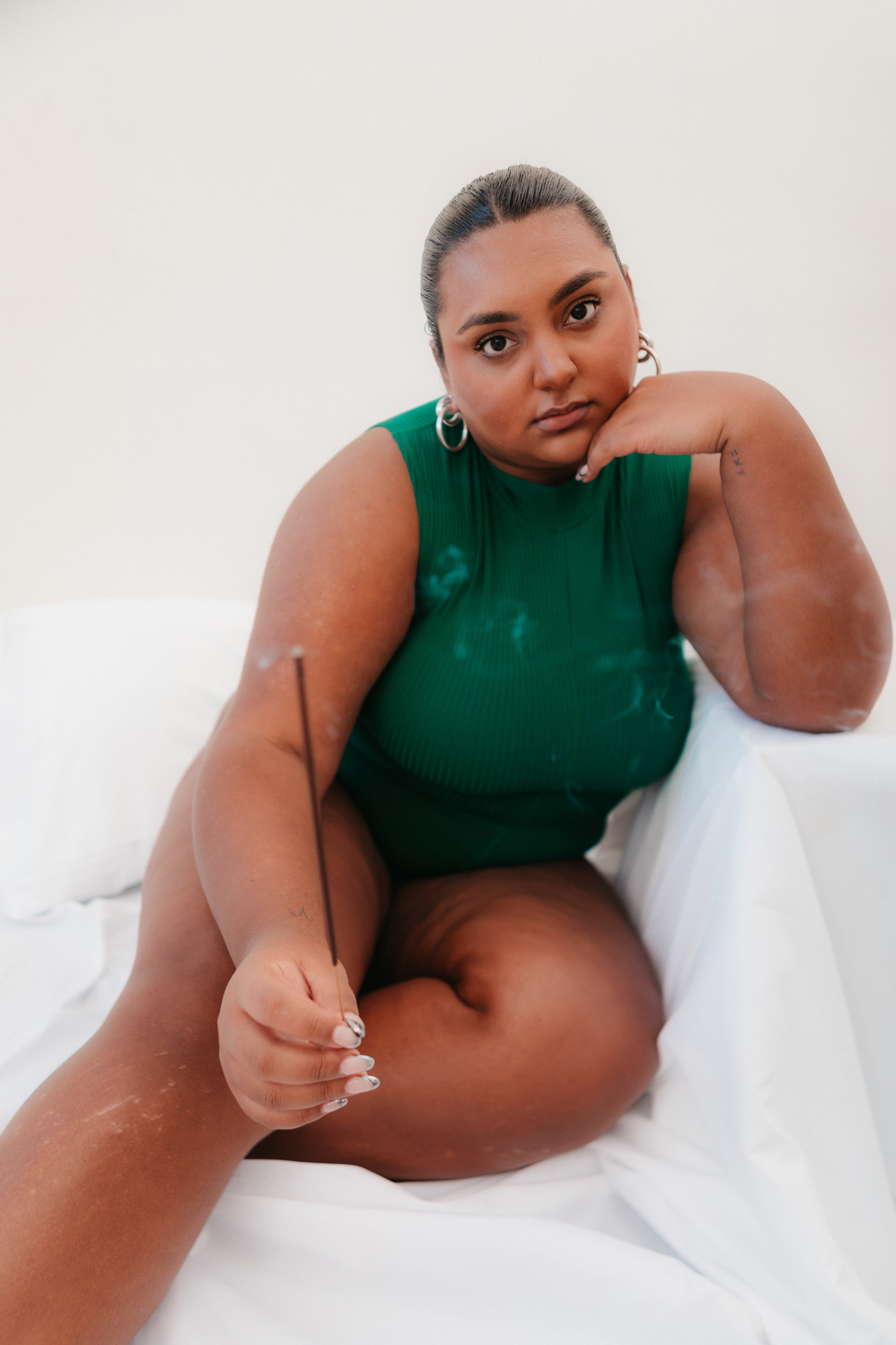Girl sits on bed wearing green loungewear, holding incense