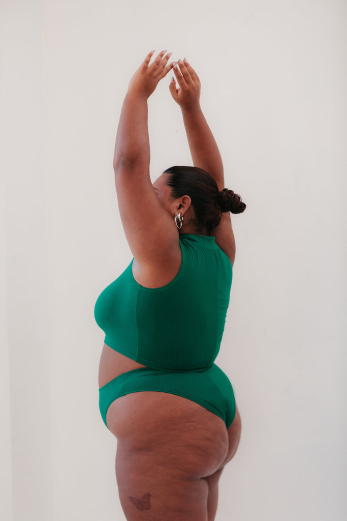 Model stands with arms up in the air, wearing a green loungewear set.