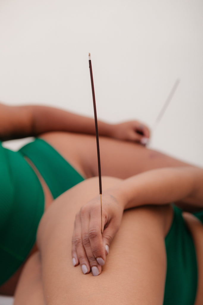 Two girls lay on a bed holding sticks of incense.